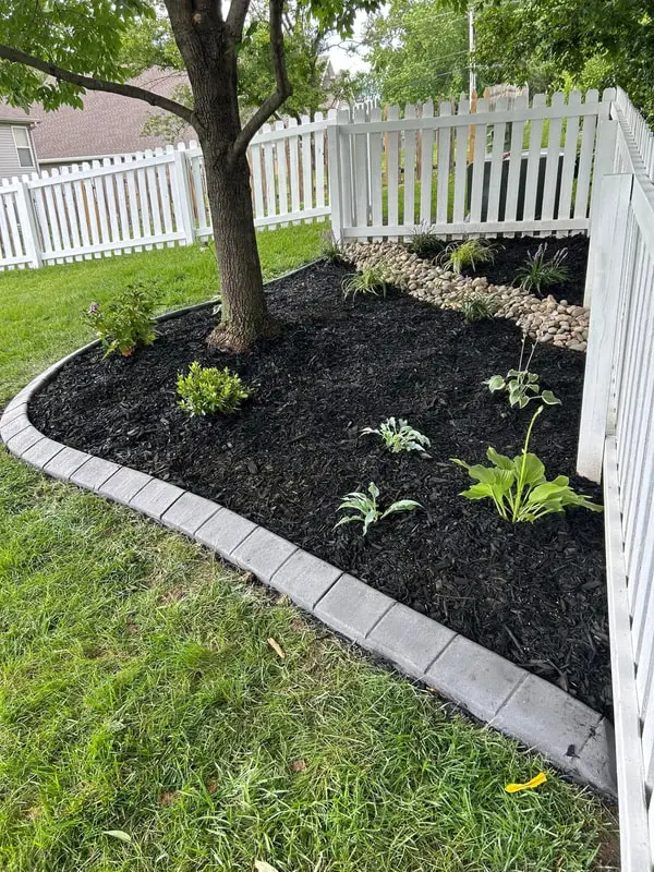 Fresh mulch bed with new plants and block edging along a white fence