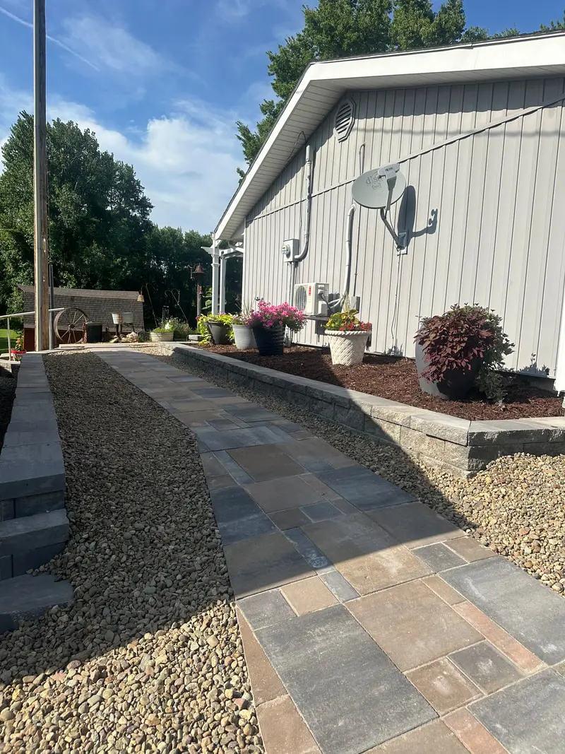 Paver walkway with rock borders beside a garage